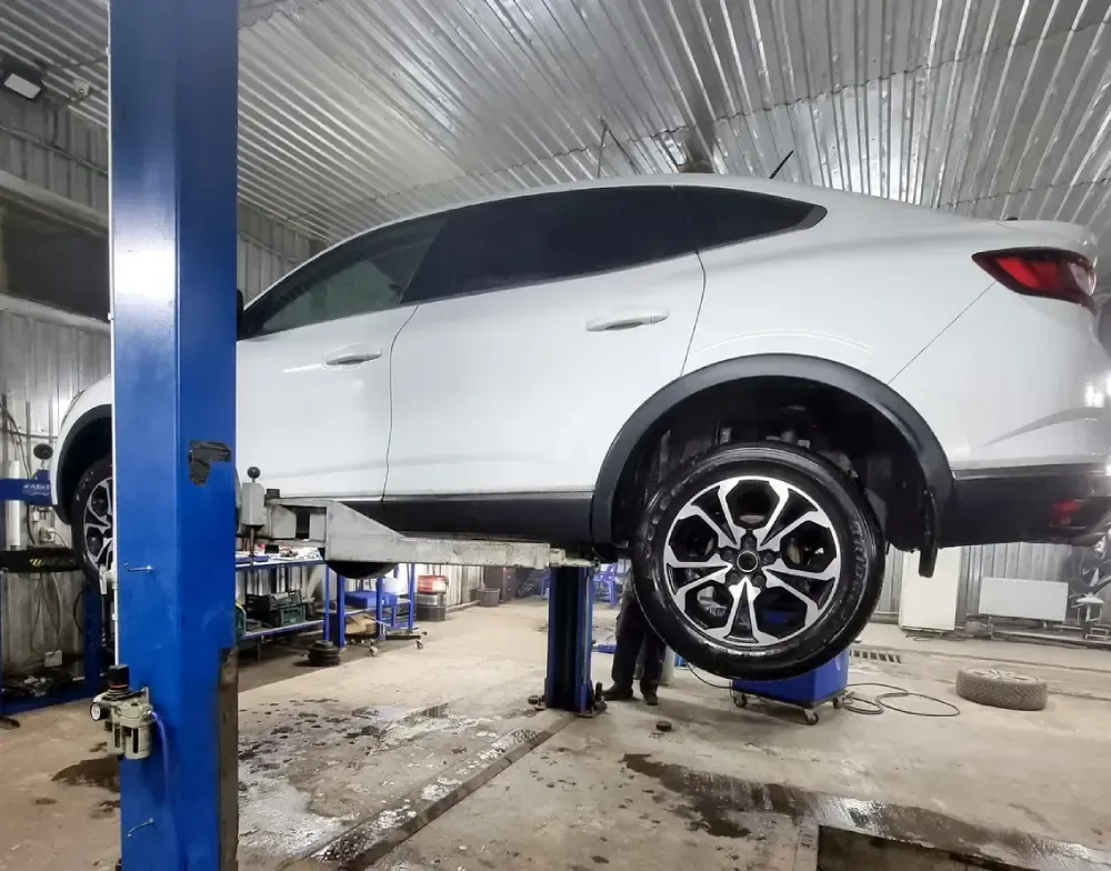 White SUV lifted on a blue hydraulic car lift in an auto repair shop, wheel visible in foreground