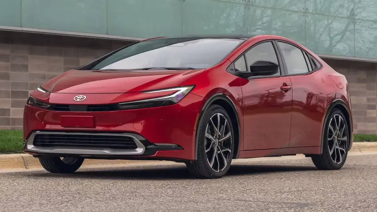 Red sports sedan parked on a road, shown in front three-quarter view against a concrete wall.