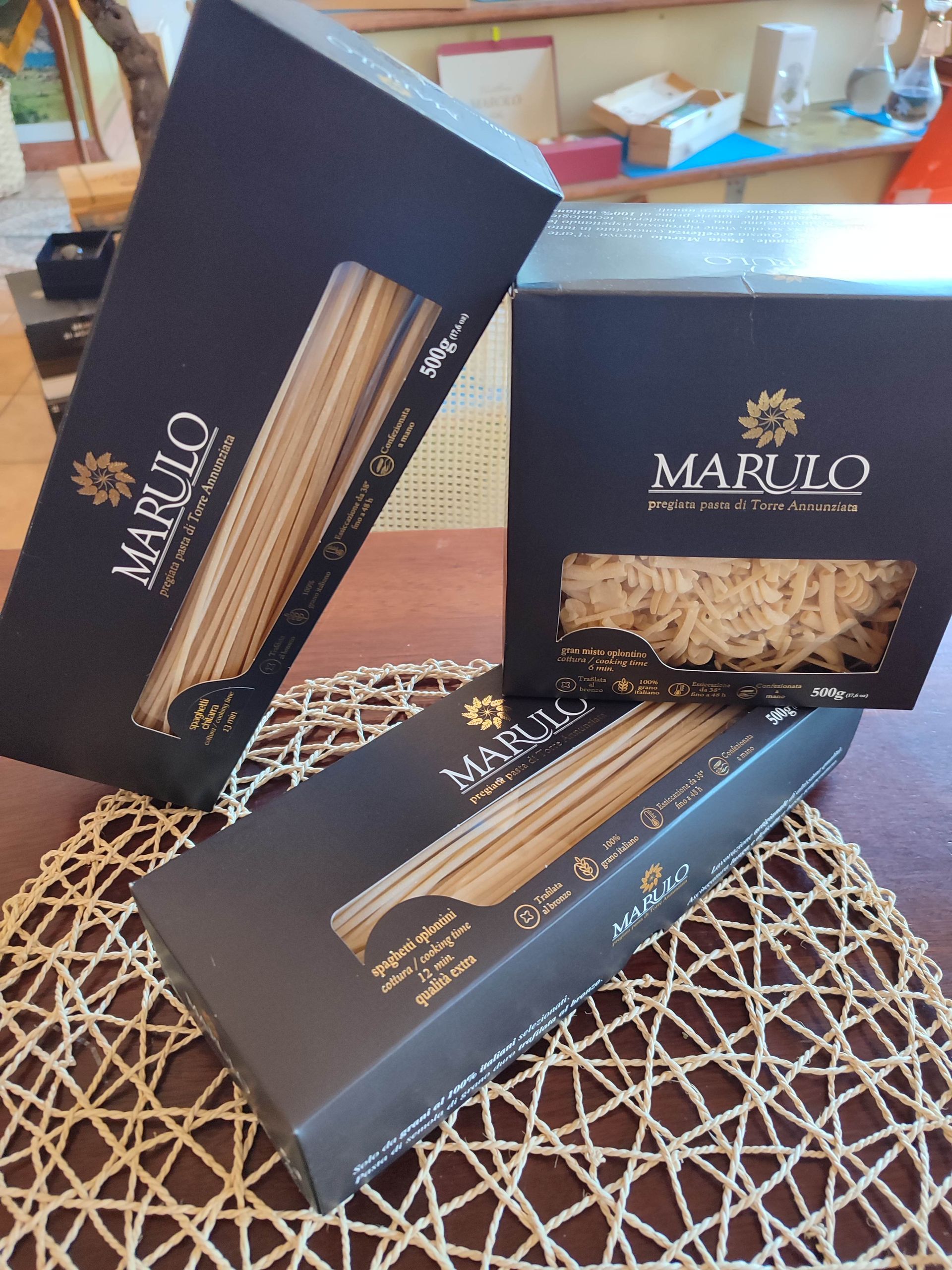 Scatole di snack Black Marloo con wafer a bastoncino rigati disposte su un vassoio intrecciato e sul tavolo