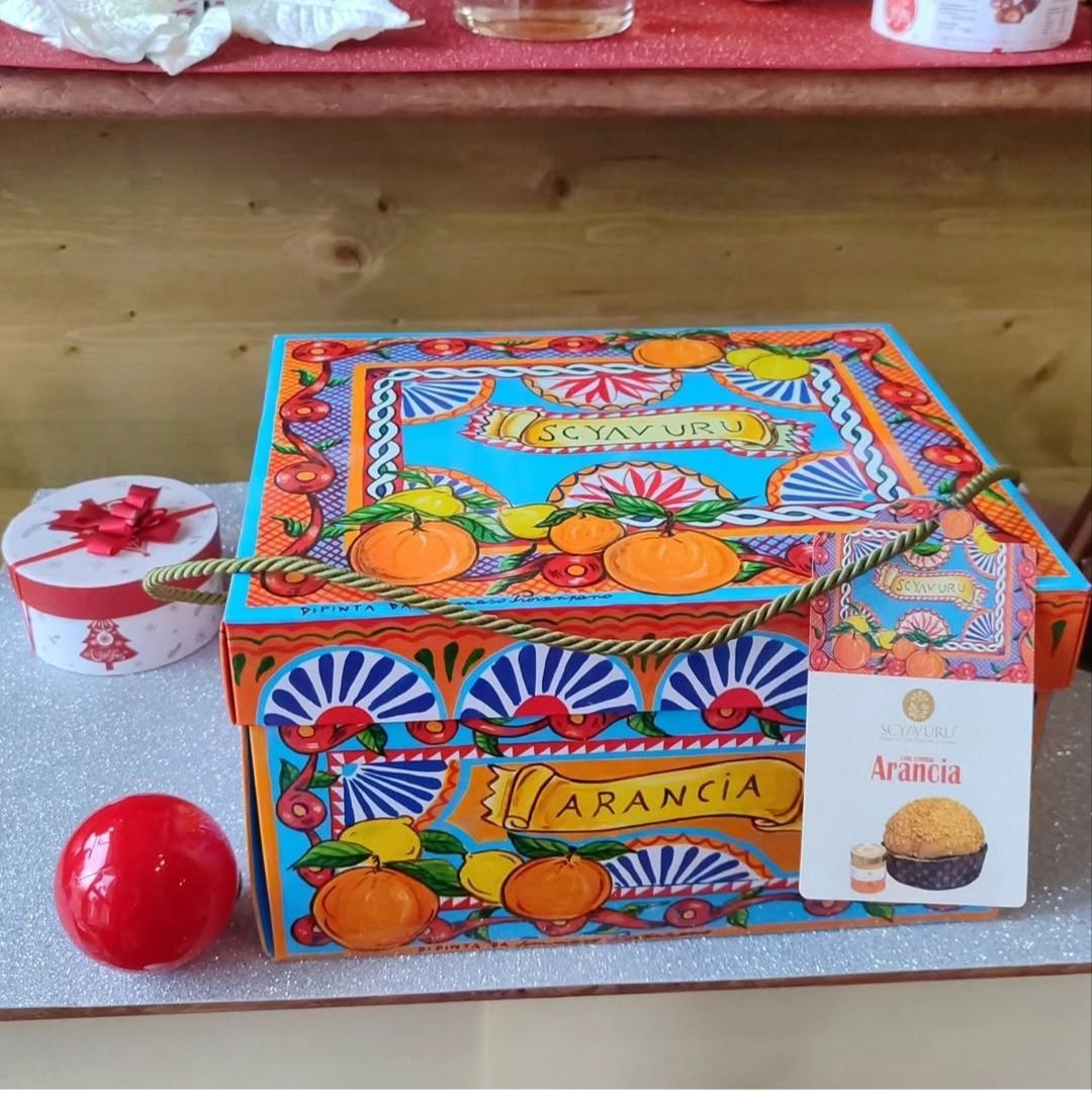 Confezione colorata a tema arancione, con un oggetto rotondo rosso e una scatolina bianca su uno scaffale
