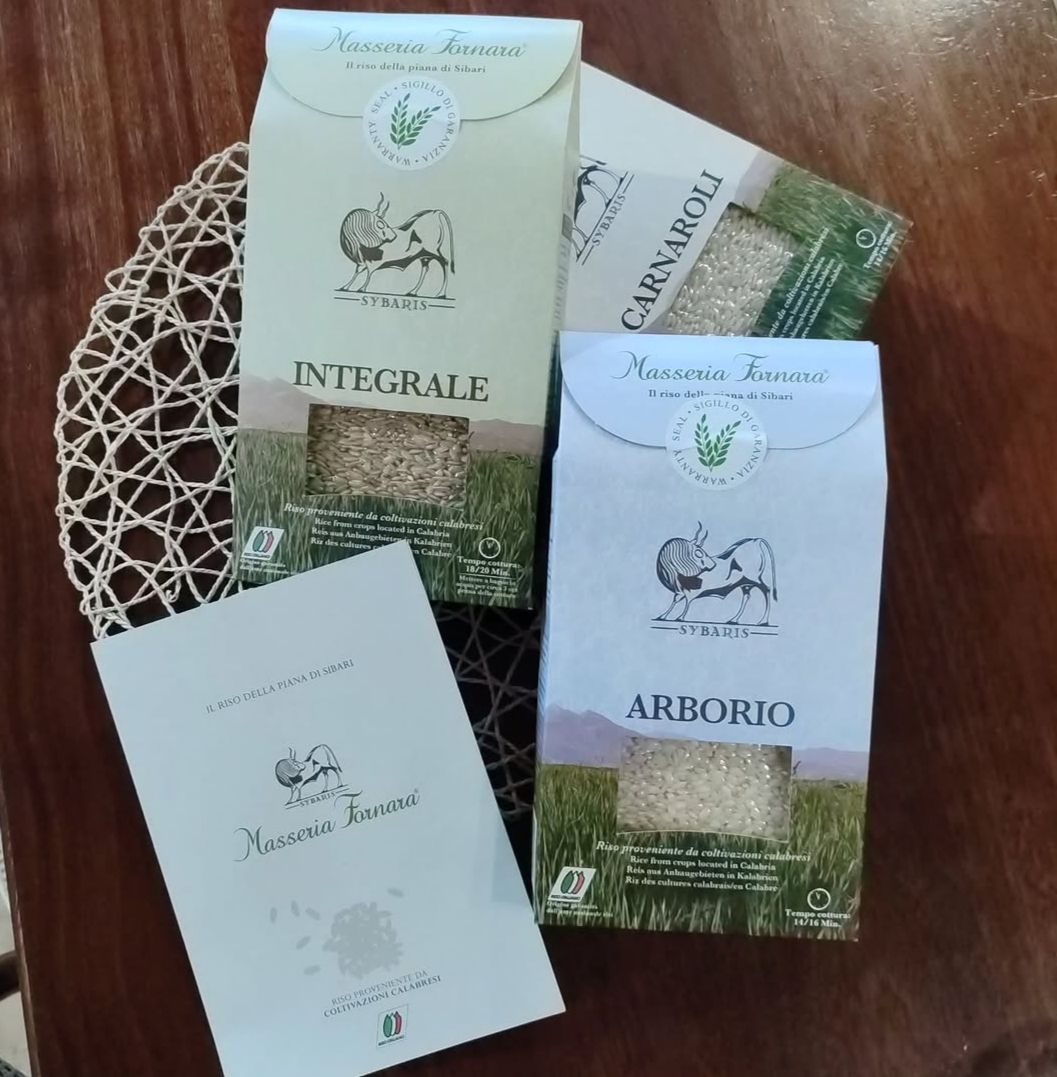 Tre confezioni di riso in un cestino di vimini su un tavolo di legno, con l’etichetta Integrale e Arborio.