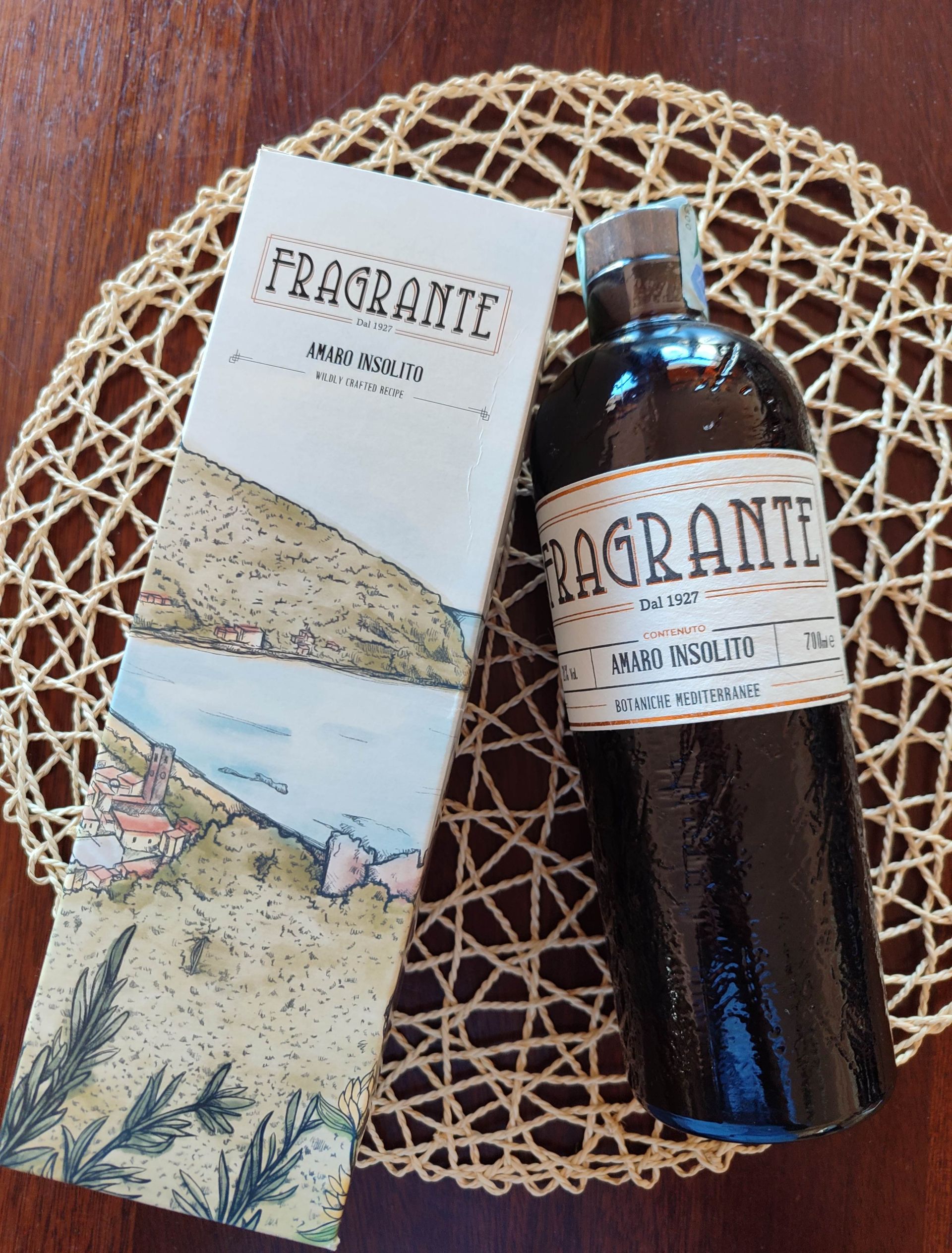 Flacone di profumo e scatola su una tovaglietta intrecciata sopra un tavolo di legno.