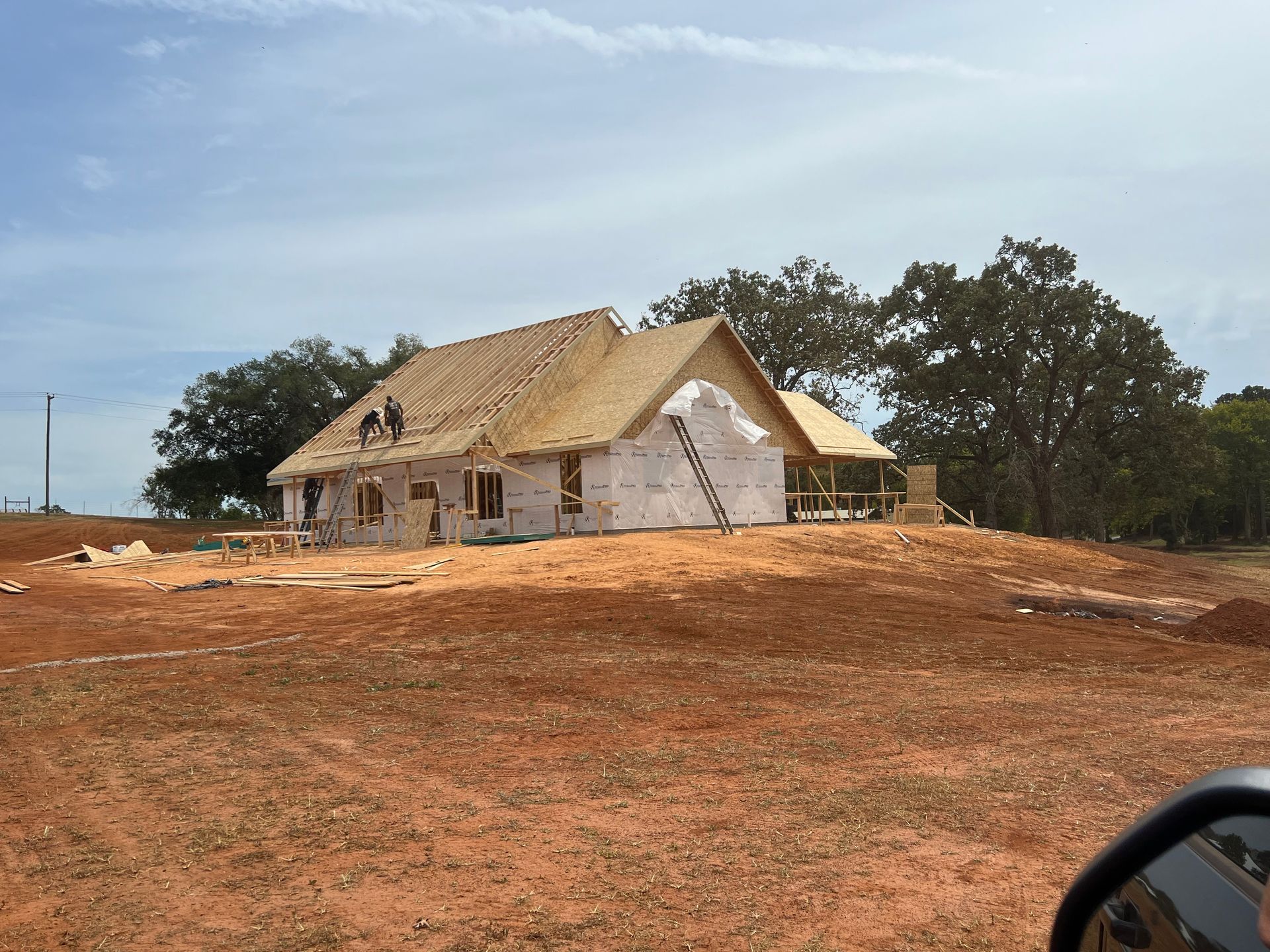 Partially built house with a thatched roof on a red dirt lot under a cloudy sky