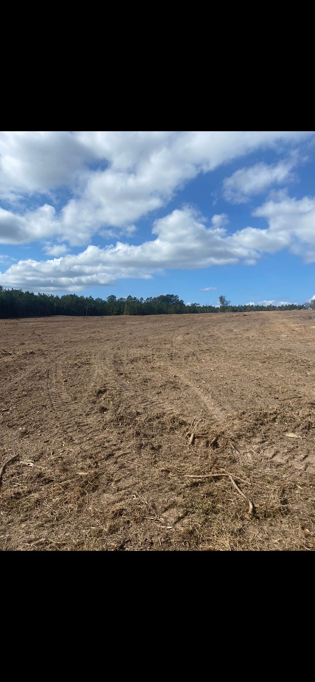 Plowed brown field under a bright blue sky with scattered white clouds