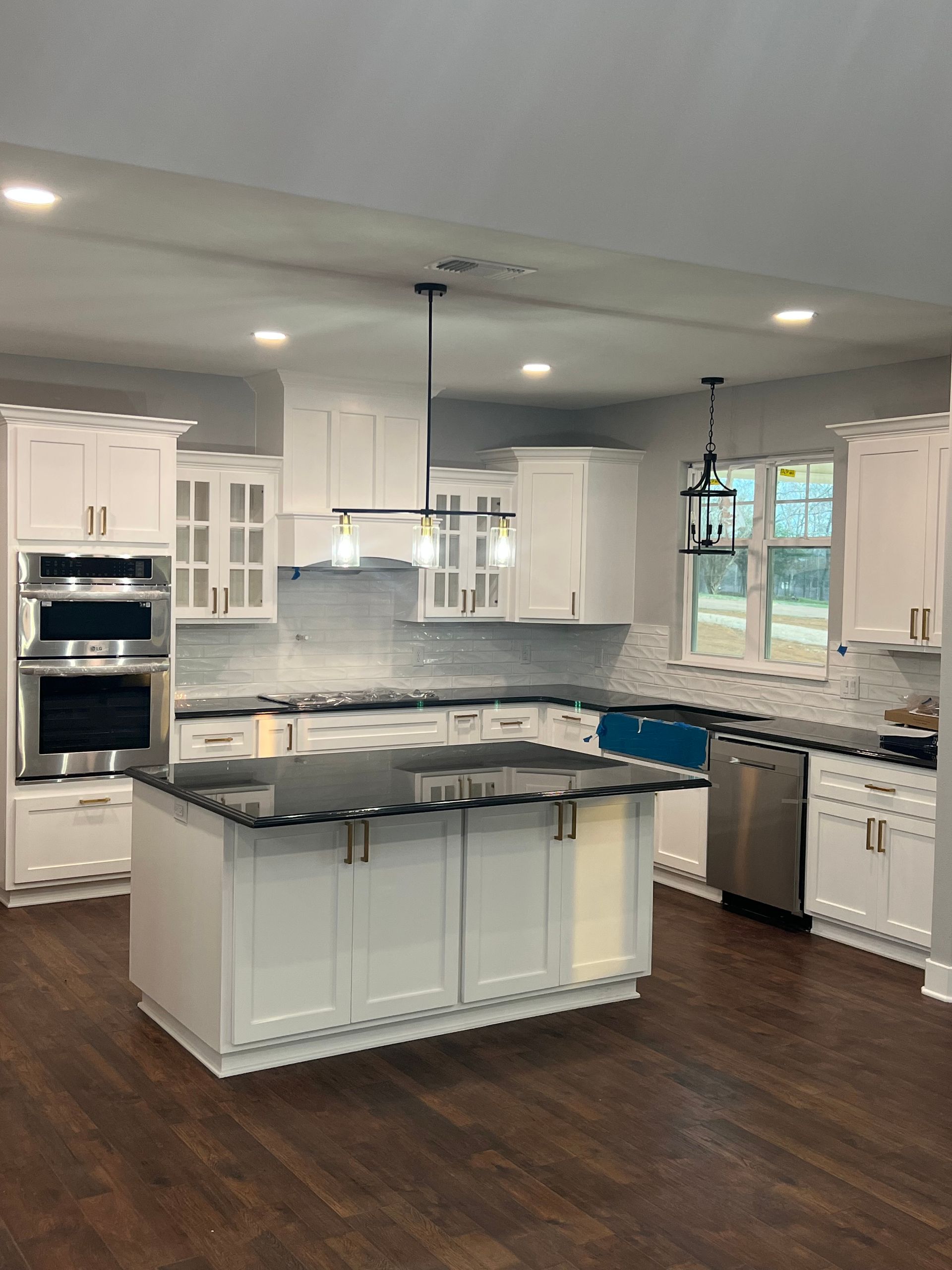 Modern kitchen with white cabinets, dark island countertop, stainless appliances, pendant lights, and wood floors