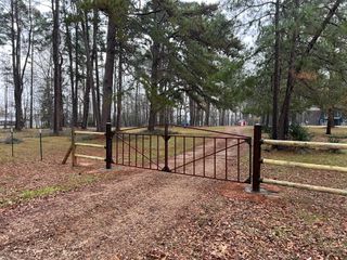 Rusty metal gate across a leaf-covered dirt path in a wooded park area