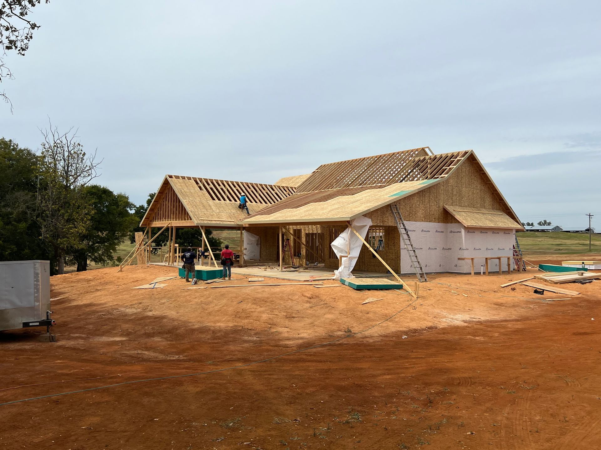 Partially built house with exposed roof framing on a dirt lot under an overcast sky