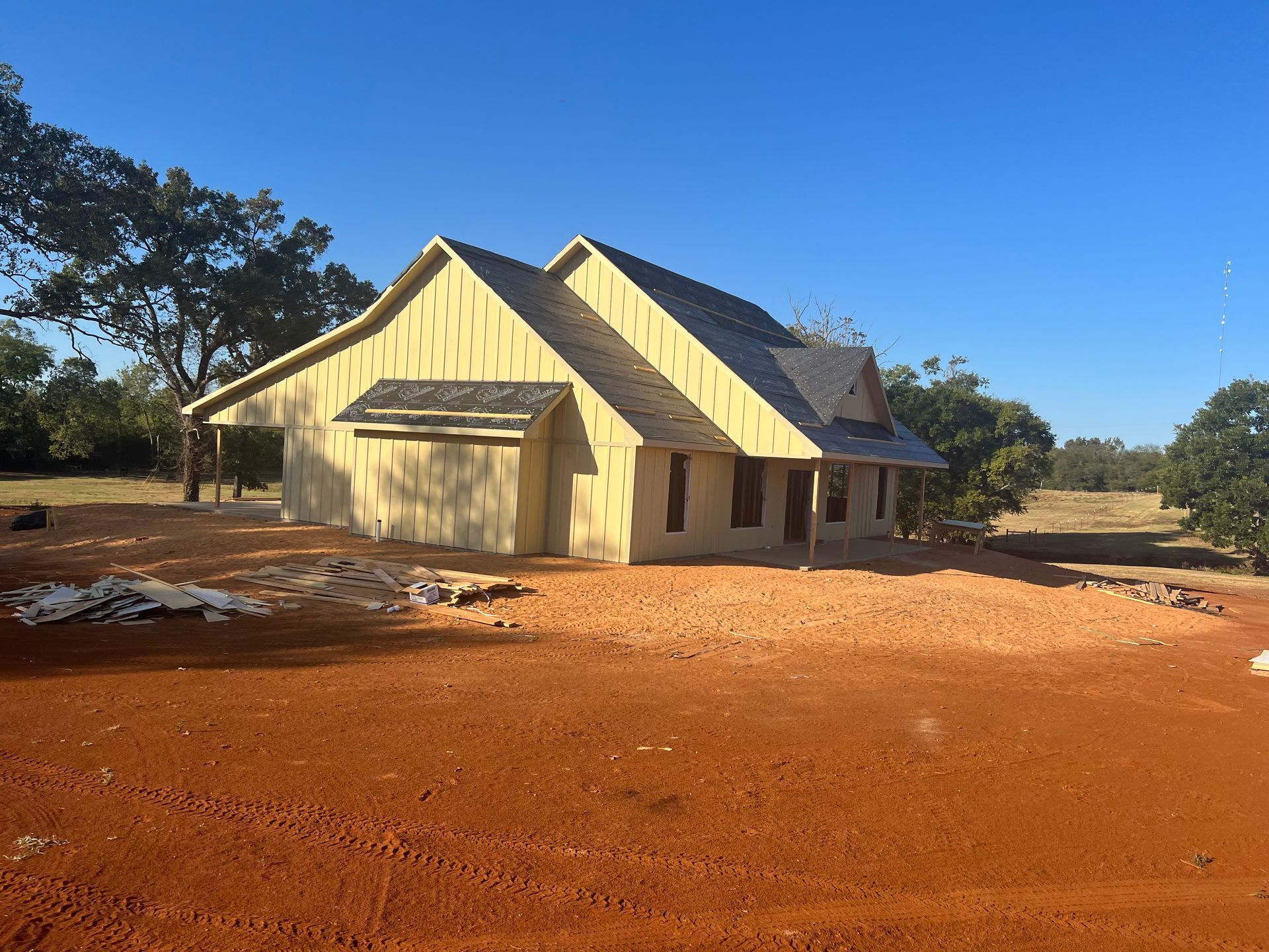 Single-story cream house with a metal roof on red dirt under a clear blue sky