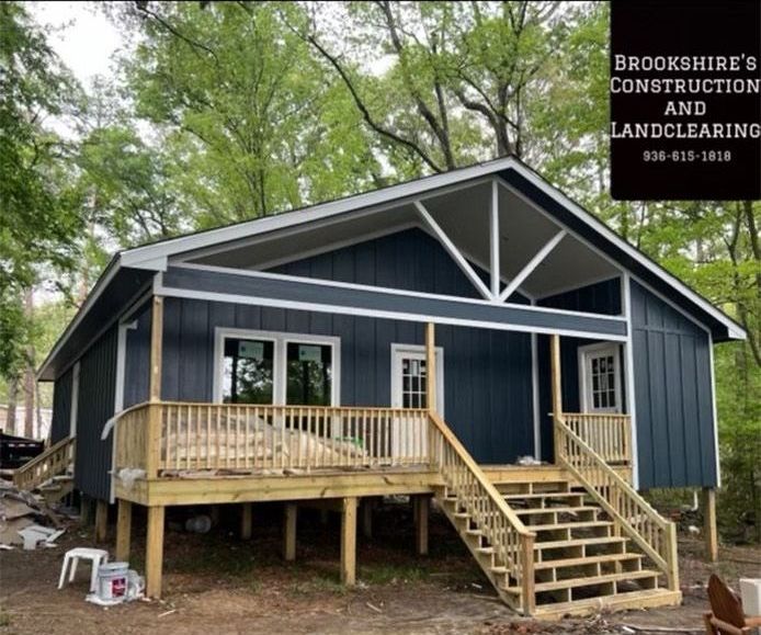 Blue house with a wooden porch and stairs, set among trees in a wooded yard