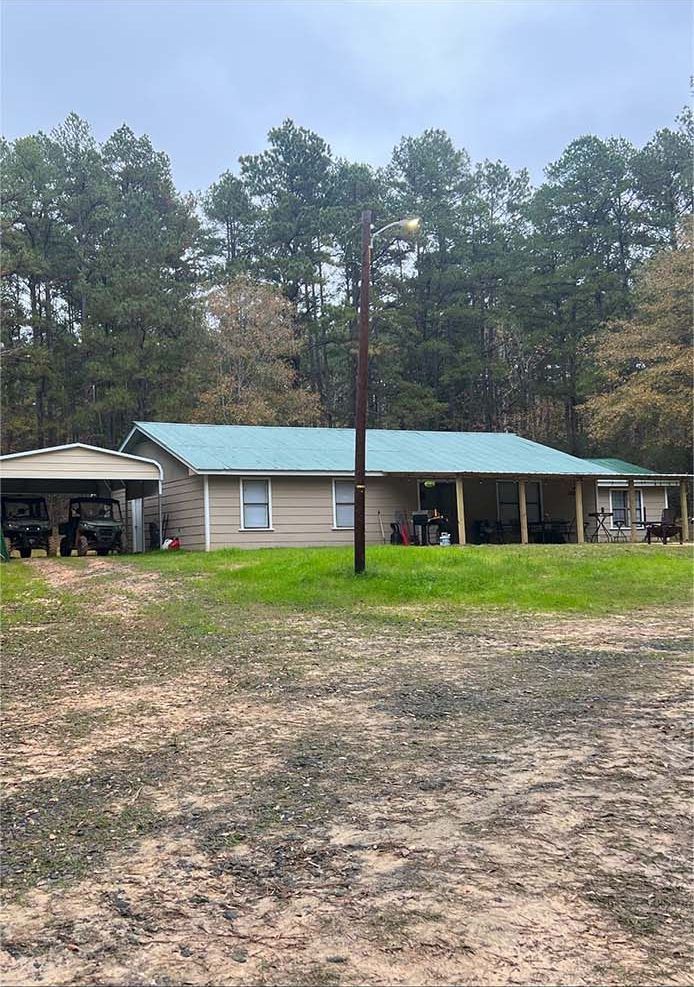 Rural single-story house with a turquoise roof, carport, and trees in the background