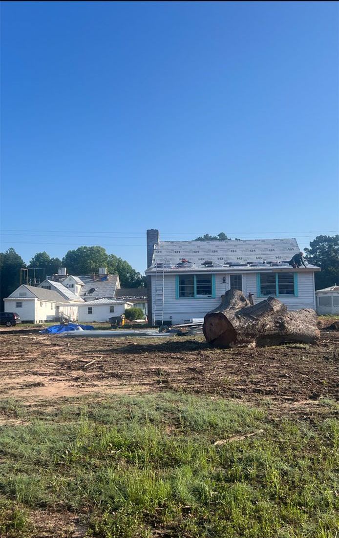 Small white house with blue shutters under a clear blue sky, with a cleared dirt lot in the foreground.