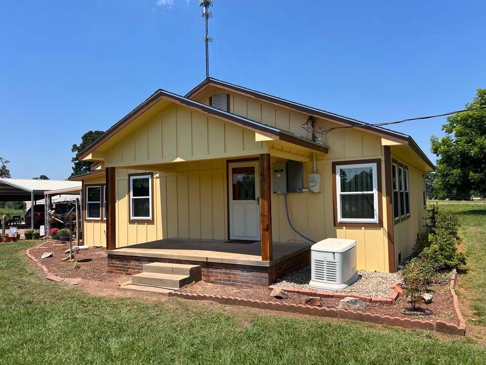 Small yellow house with a front porch, brick steps, and a window air conditioner under a clear blue sky