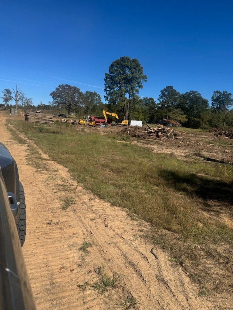 Dirt road beside a field with excavators and debris under a clear blue sky