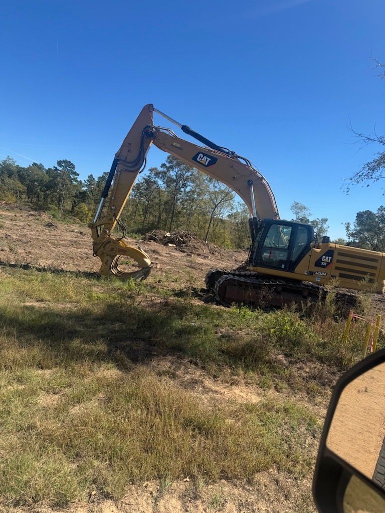 Yellow excavator digging on a grassy hillside under a clear blue sky.