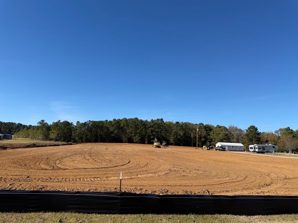 Cleared dirt lot under blue sky with trees and a black silt fence in front