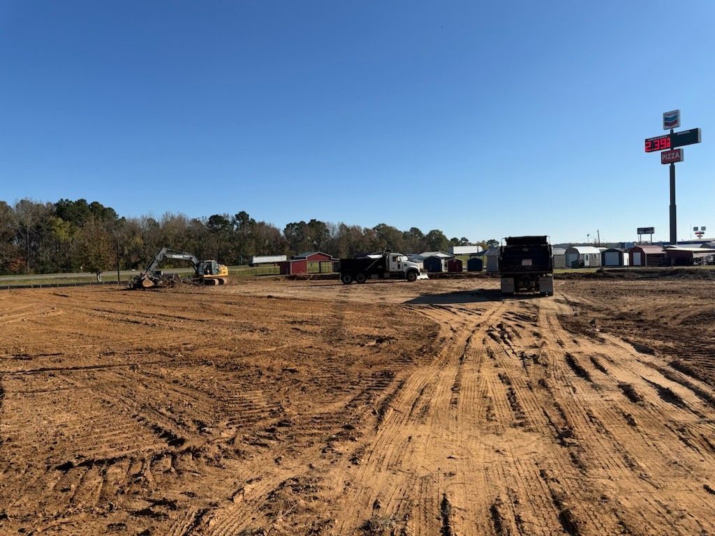 Dirt lot with parked work vehicles and a tall roadside sign under a clear sky
