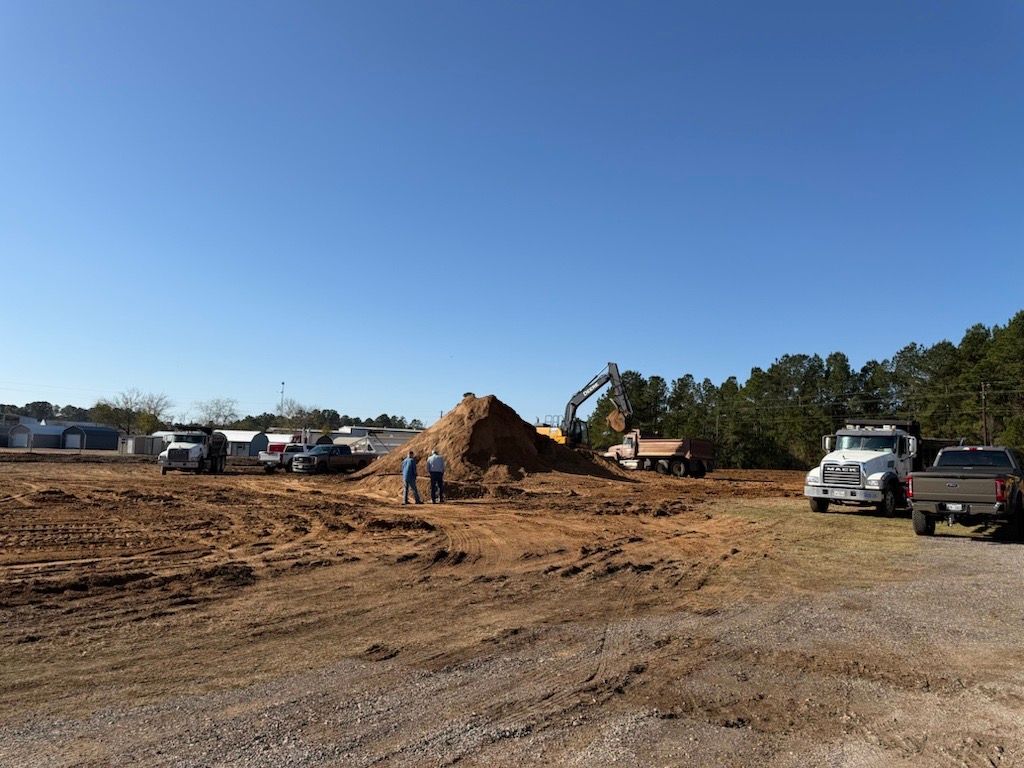 Construction site with excavator, dirt mound, workers, and trucks under a clear blue sky