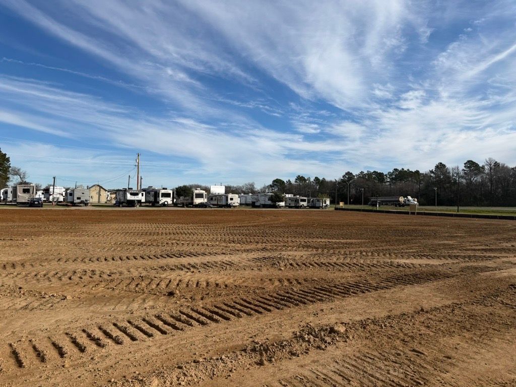 Wide sandy field under a blue sky with wispy clouds, houses and trees along the horizon.
