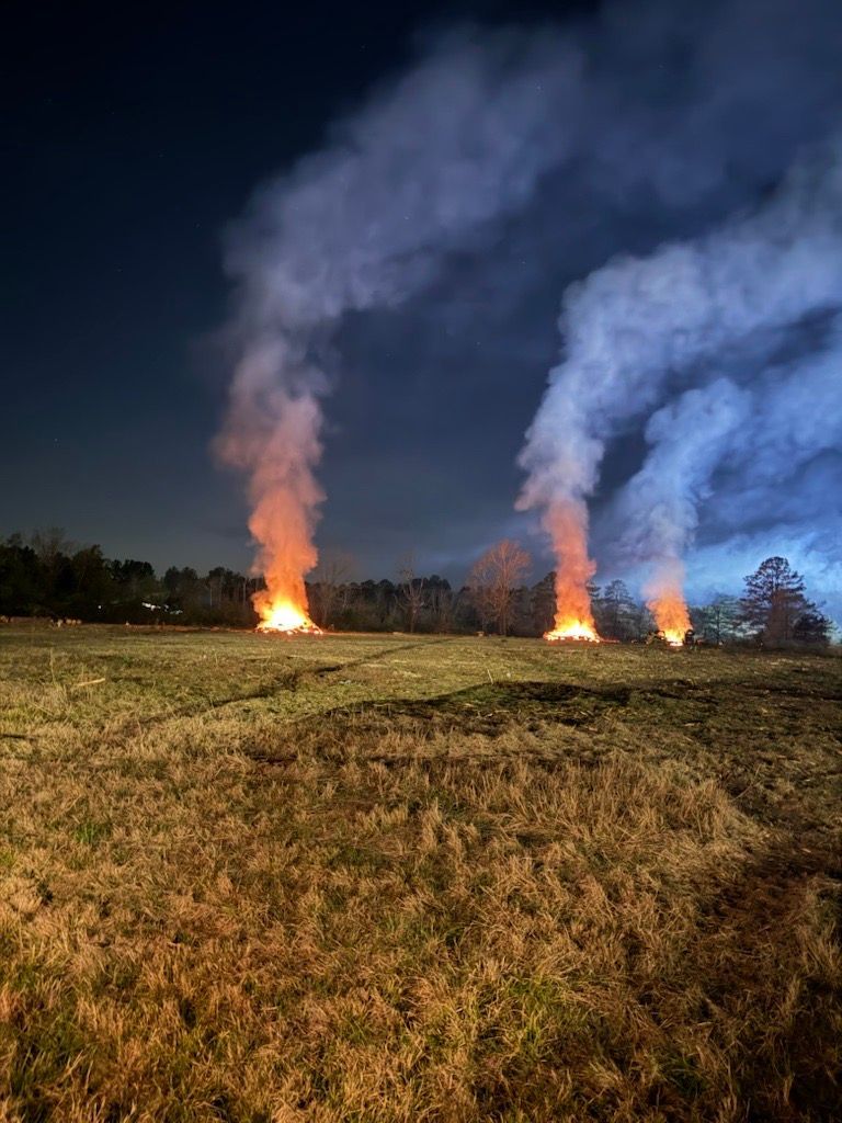 Two small fires on a grassy field at night, each sending up a tall column of smoke.
