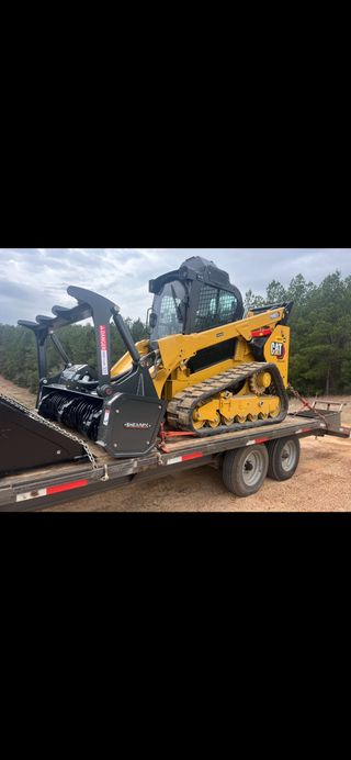 Yellow compact excavator on a trailer at a construction site with dirt and trees nearby