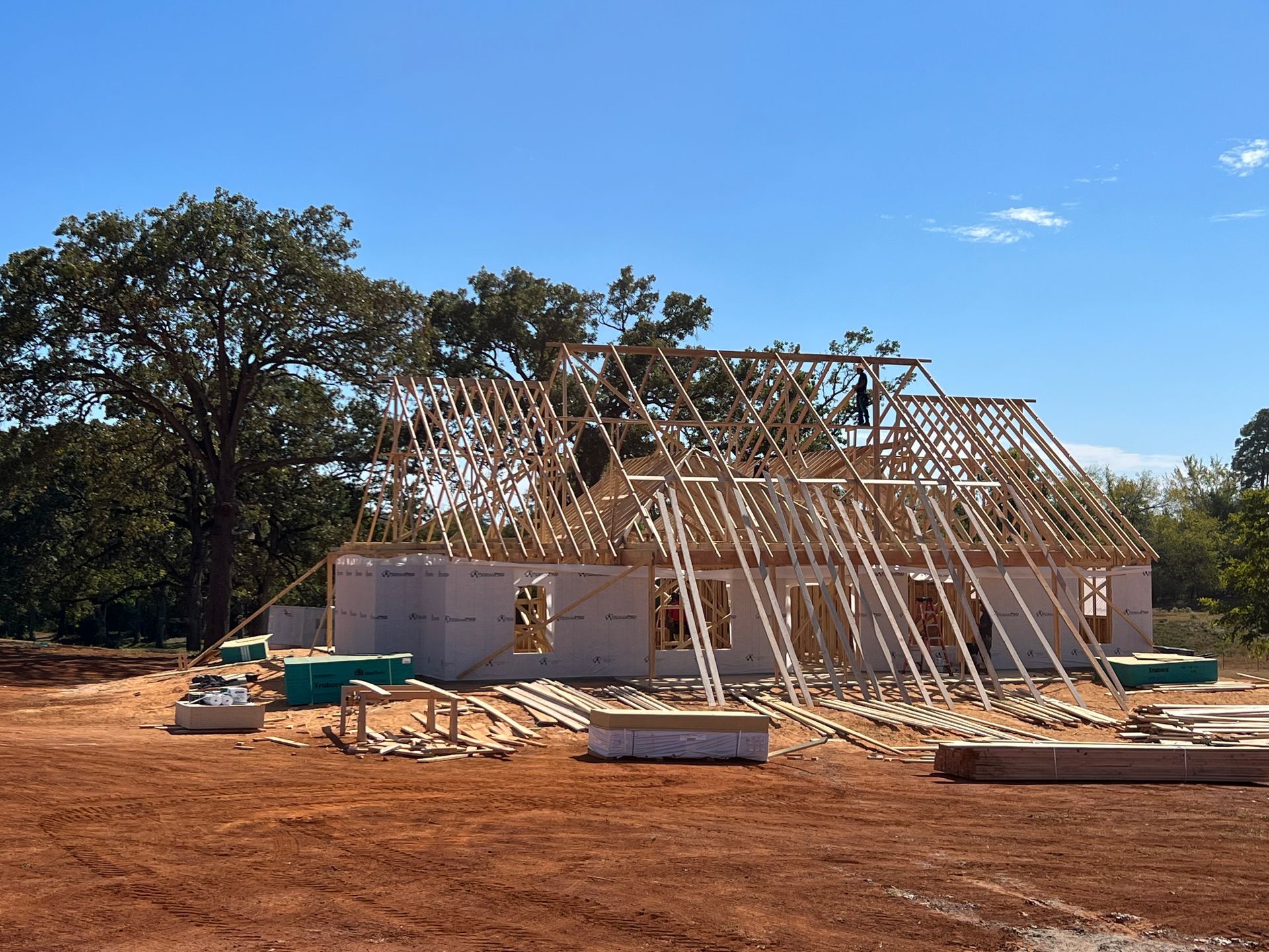 Partially built house with wooden framing on a dirt lot under a blue sky