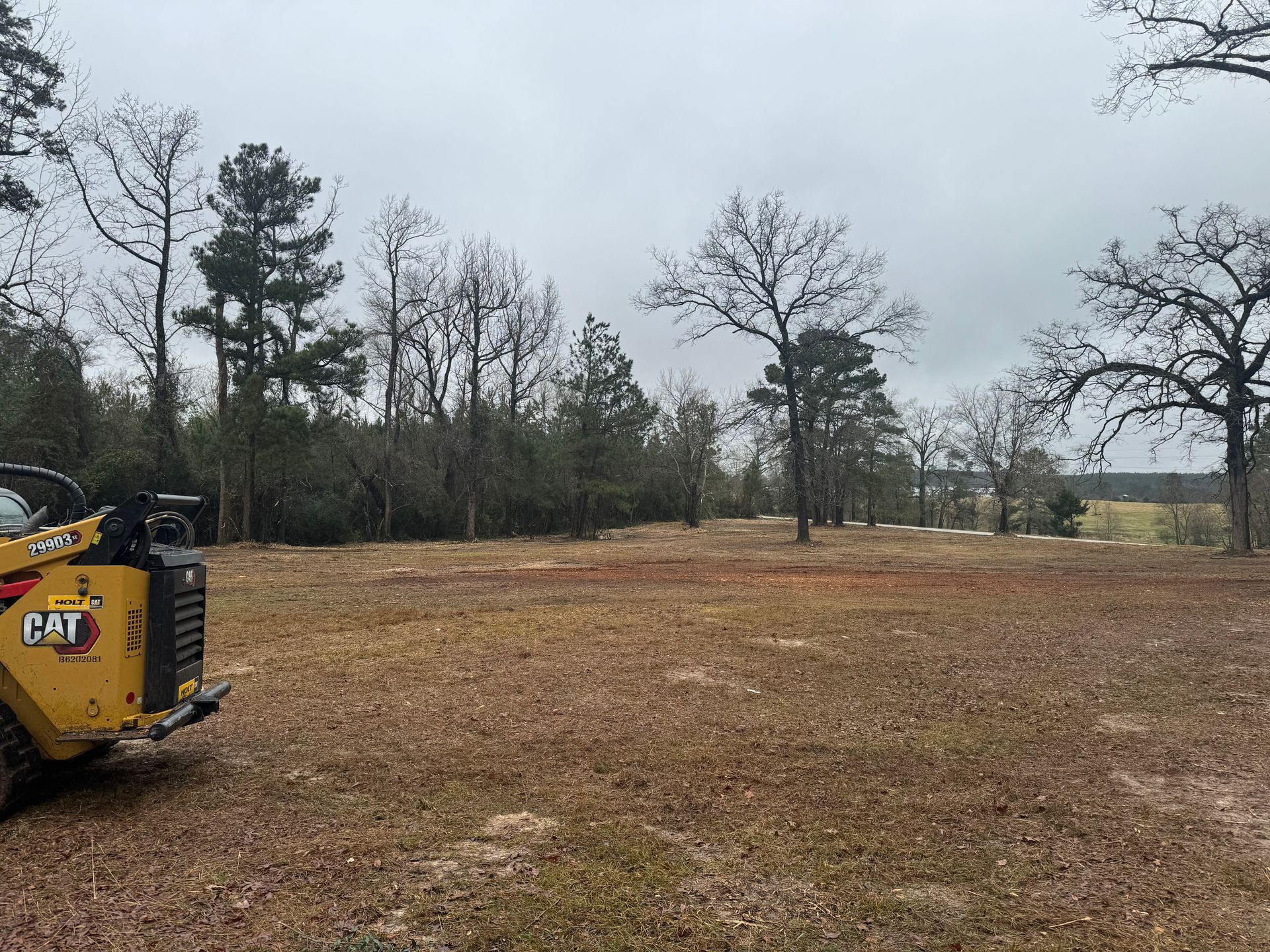 Construction site with a yellow CAT vehicle on a cleared field under an overcast sky