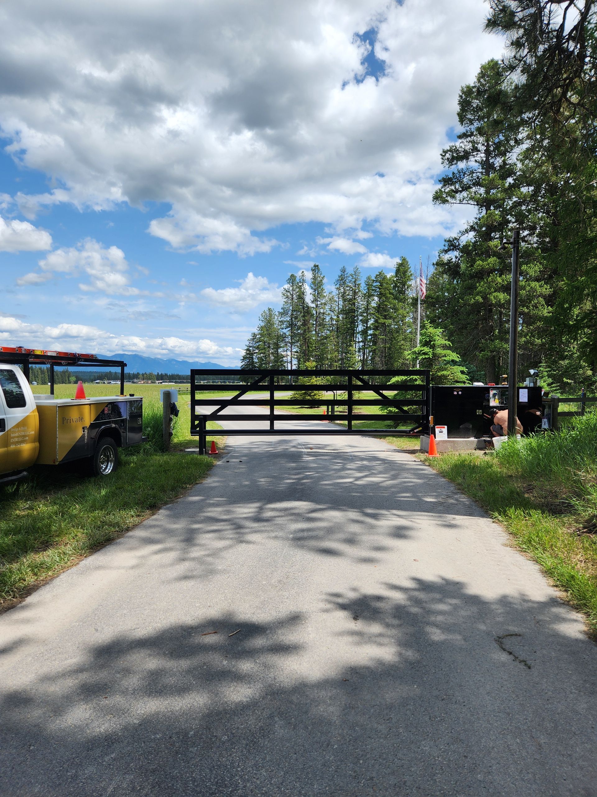 A metal gate is sitting on the side of a dirt road.