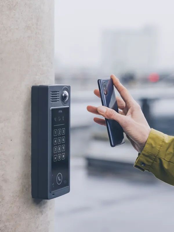 A person is holding a cell phone in front of a doorbell.