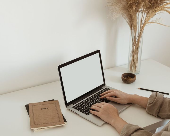 Uma pessoa está digitando em um laptop com uma tela branca.