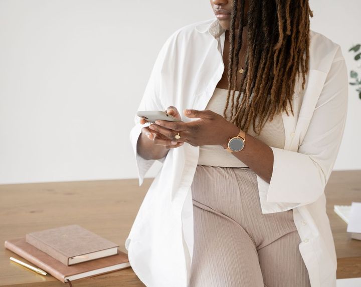 Uma mulher de jaleco branco está sentada à mesa segurando um celular.