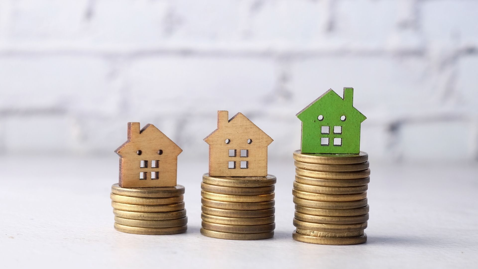 Three stacks of coins with wooden houses on top of them.