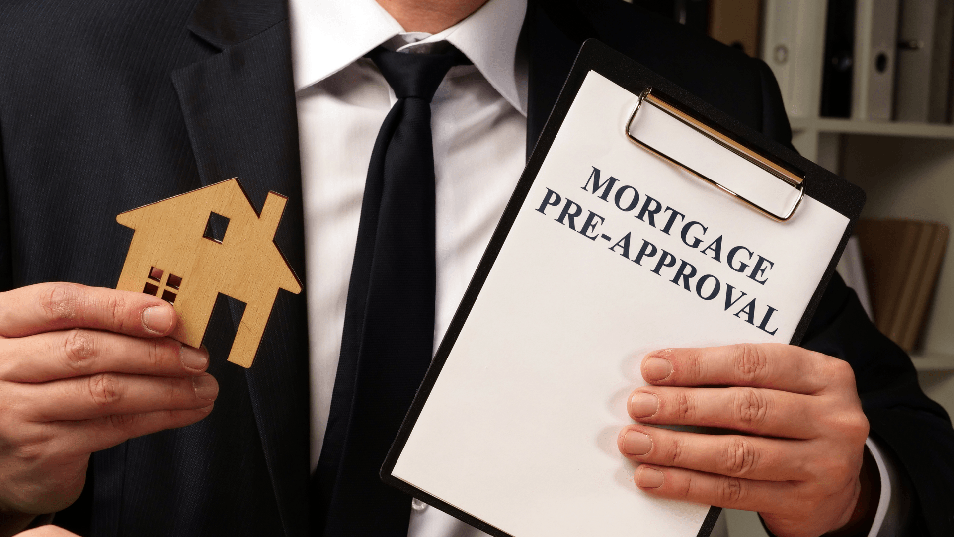 A man in a suit and tie is holding a clipboard with a mortgage pre-approval on it.