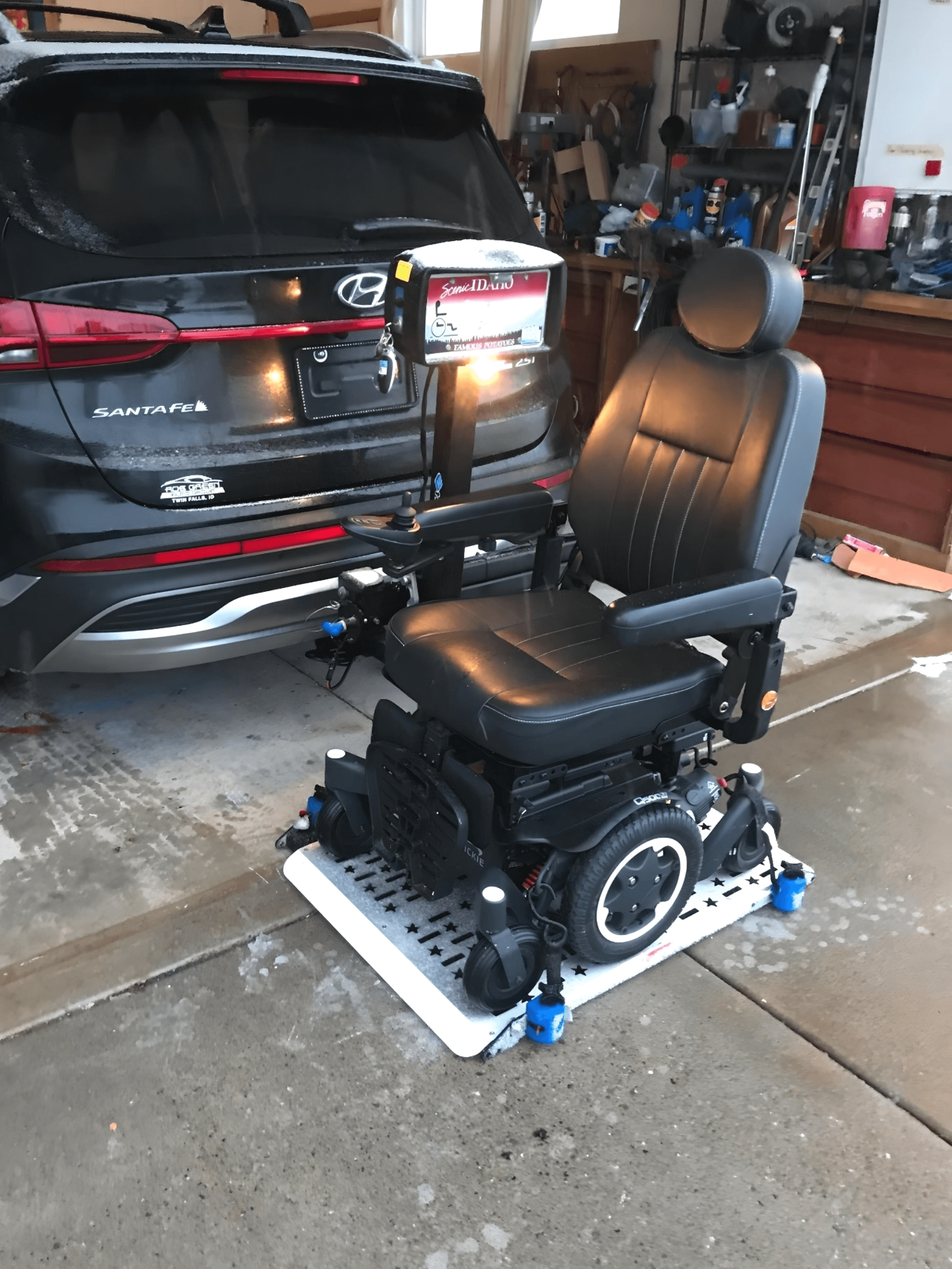A mobility chair is sitting on a tray in front of a car in a garage.