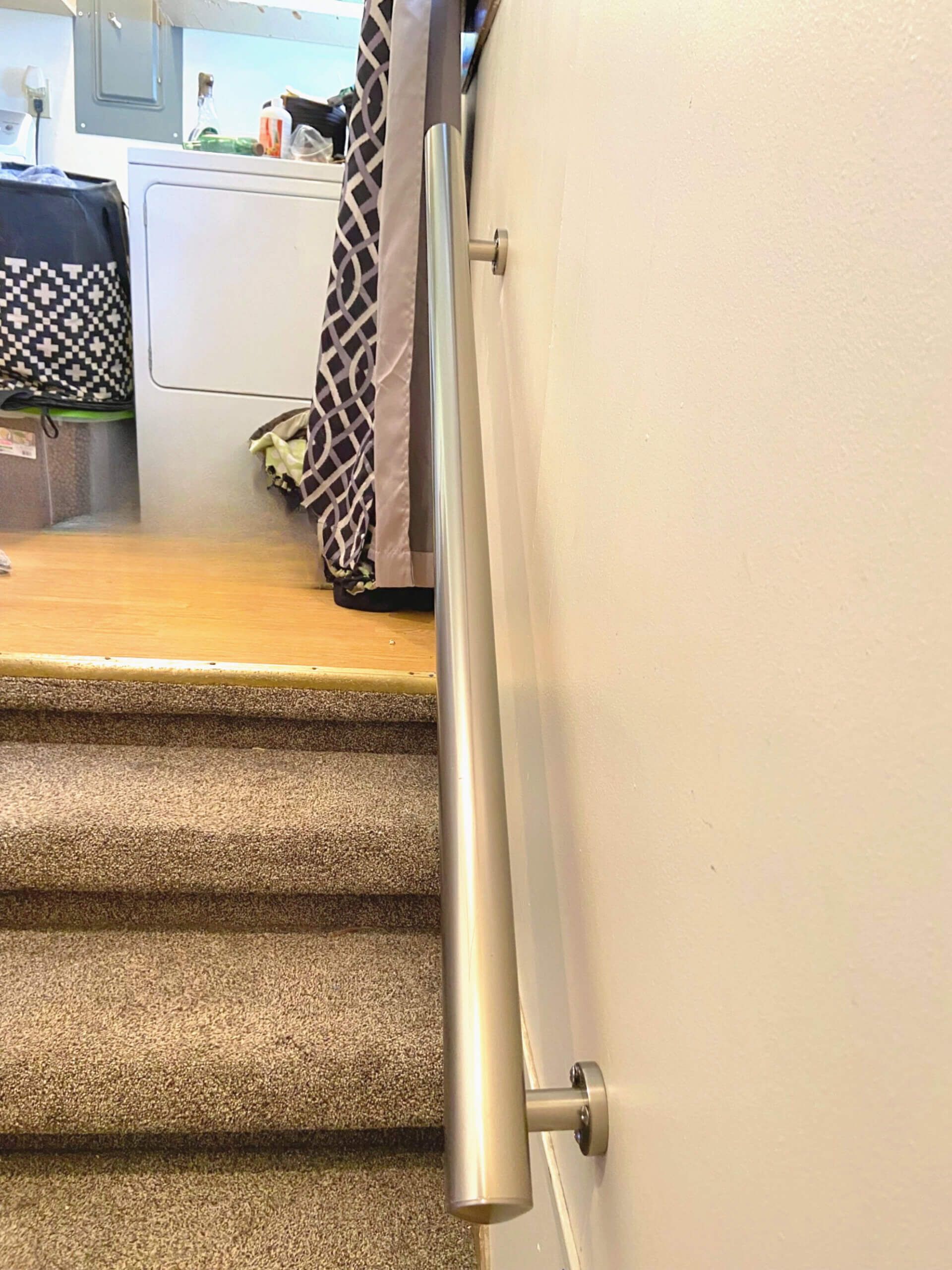 Staircase with carpeted steps and a metal handrail mounted on a white wall.