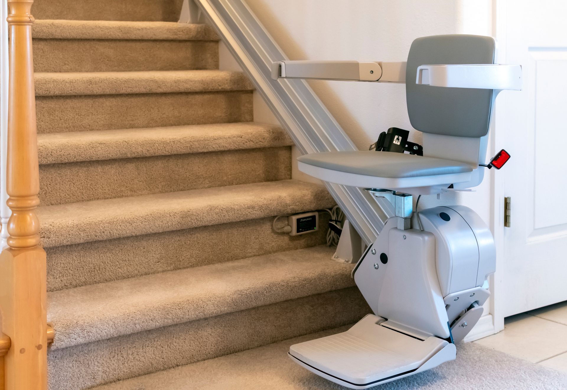 Stair lift chair installed on a carpeted staircase with a rail along the wall.