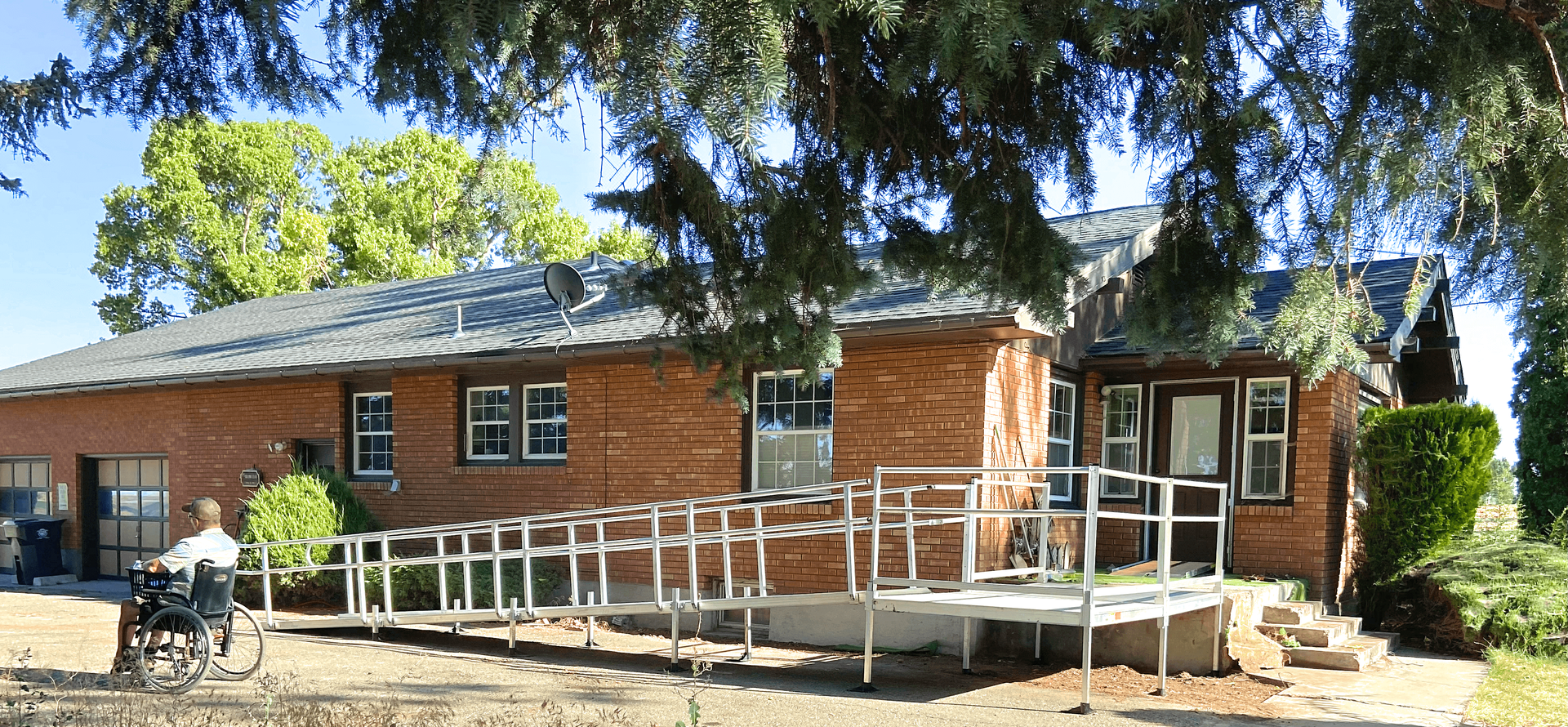 A man in a wheelchair is standing in front of a brick house with a ramp.