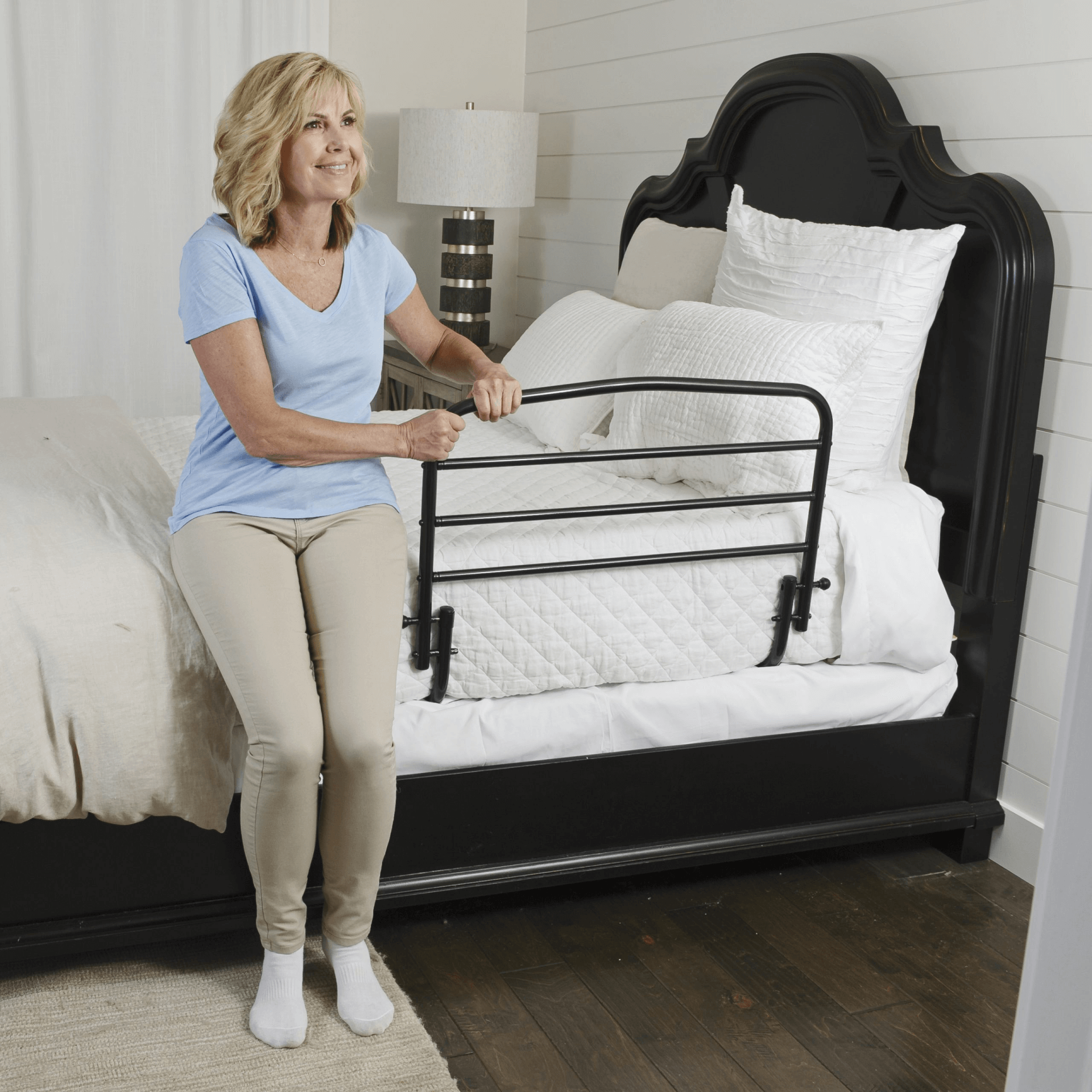 A woman is sitting on a bed holding a railing.