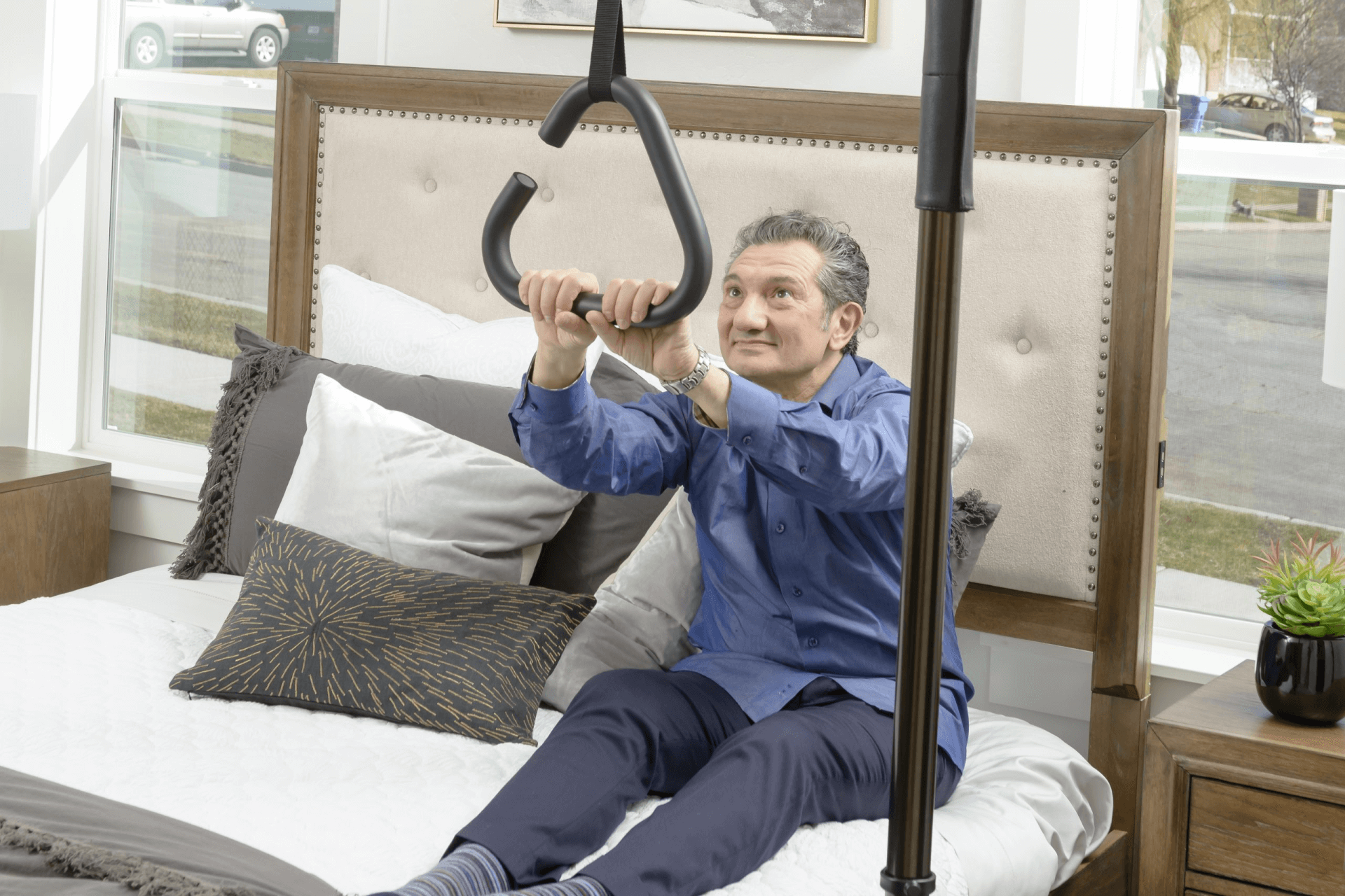 A man is sitting on a bed using a hand rail.