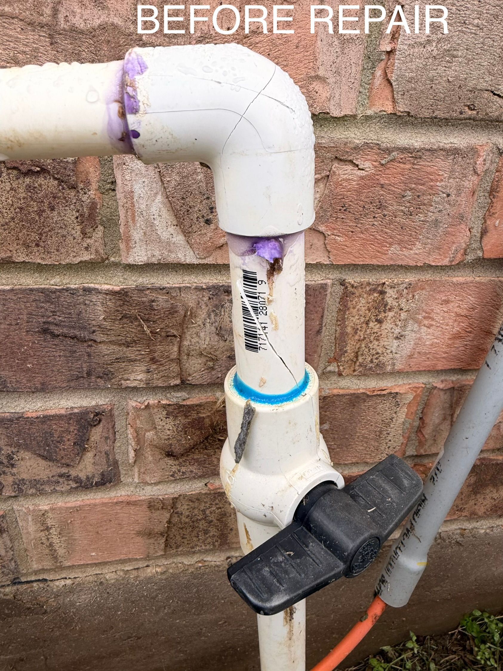 Before repair: white PVC pipe with elbow joint and black valve against a brick wall.