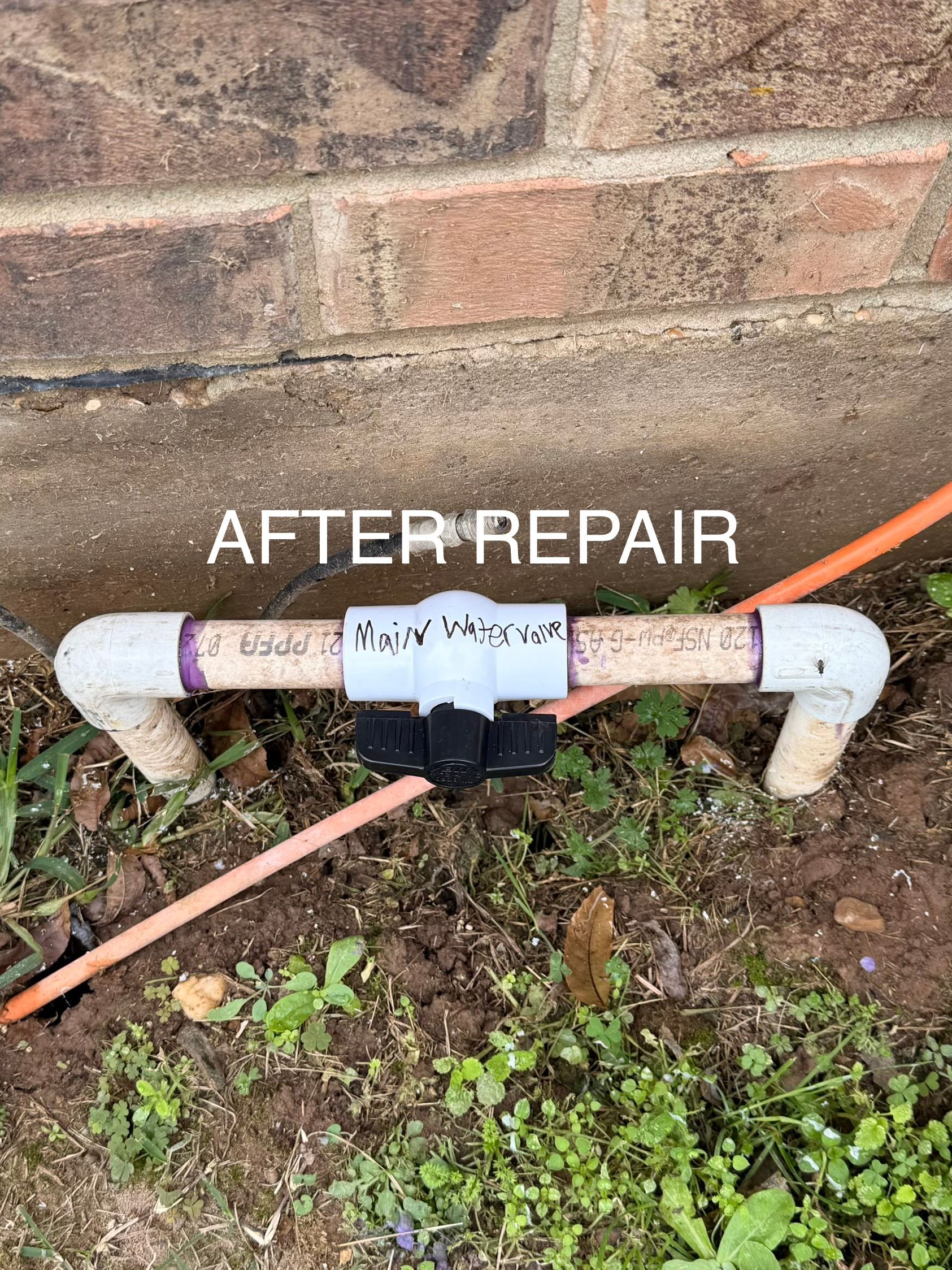 After repair, white PVC pipe joint by brick wall with orange cable nearby.