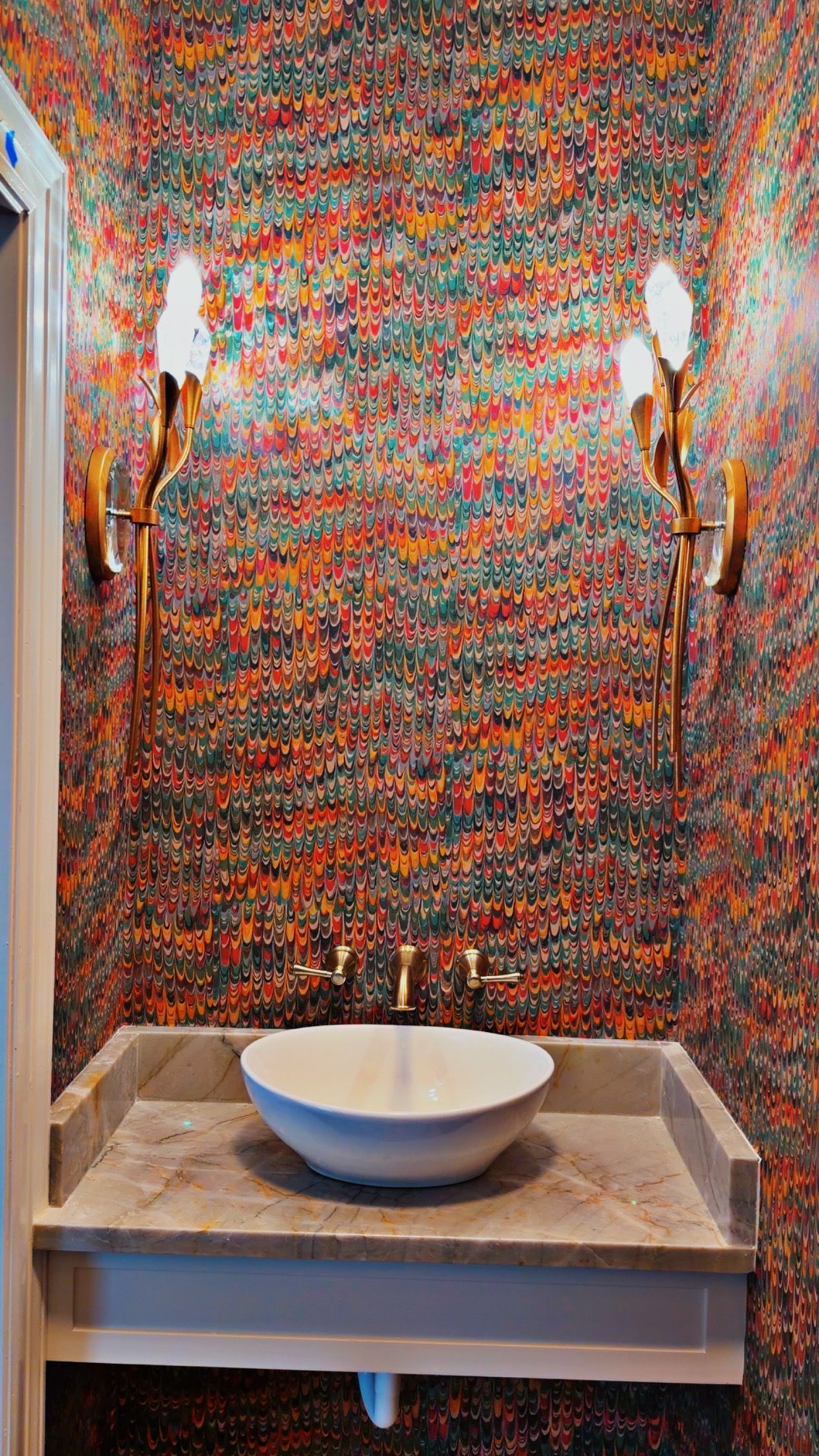 Colorful mosaic-tiled alcove with a central sink and wall sconces on either side