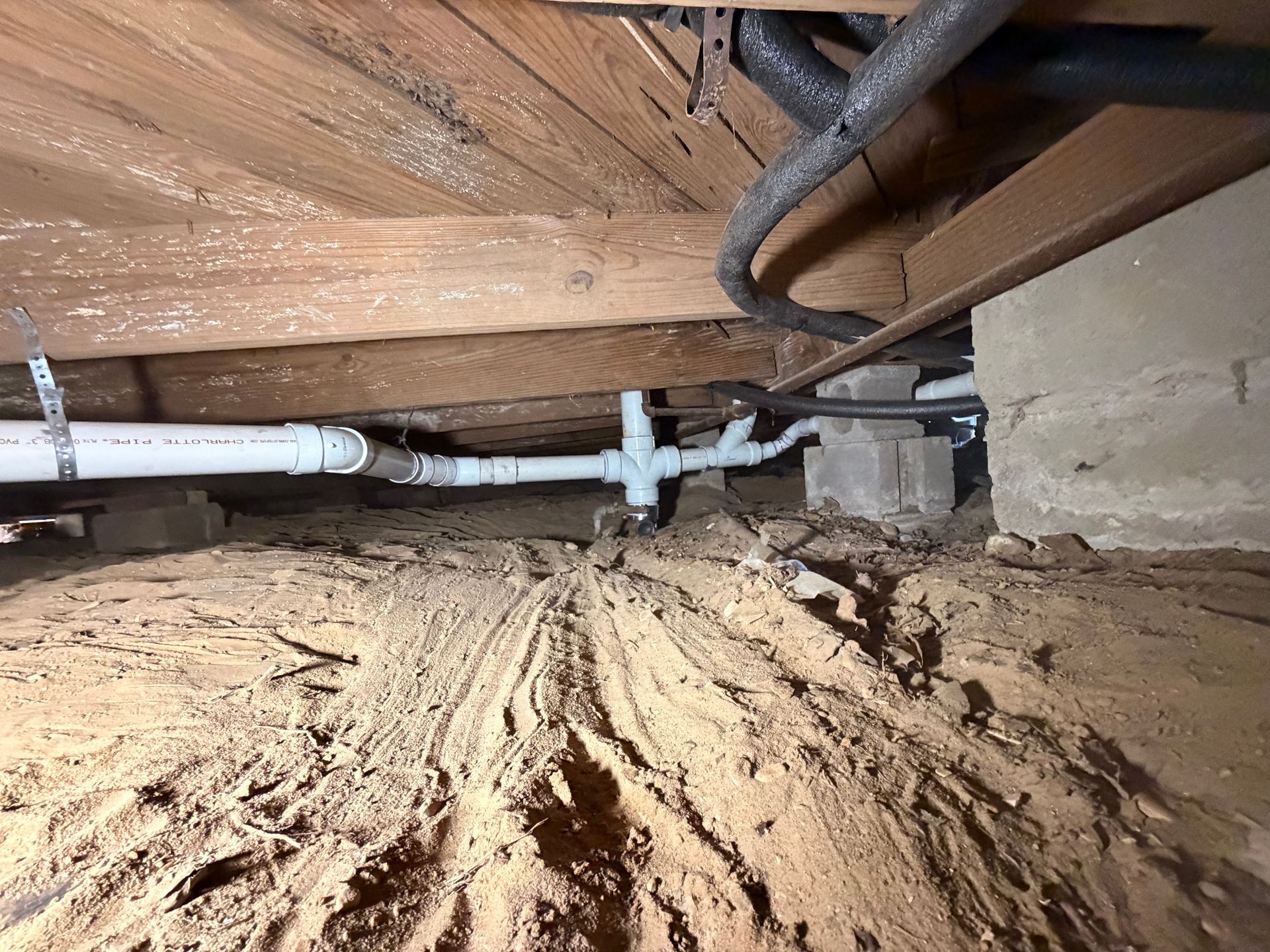 Crawlspace with exposed pipes, dirt floor, and wooden joists above a concrete foundation wall