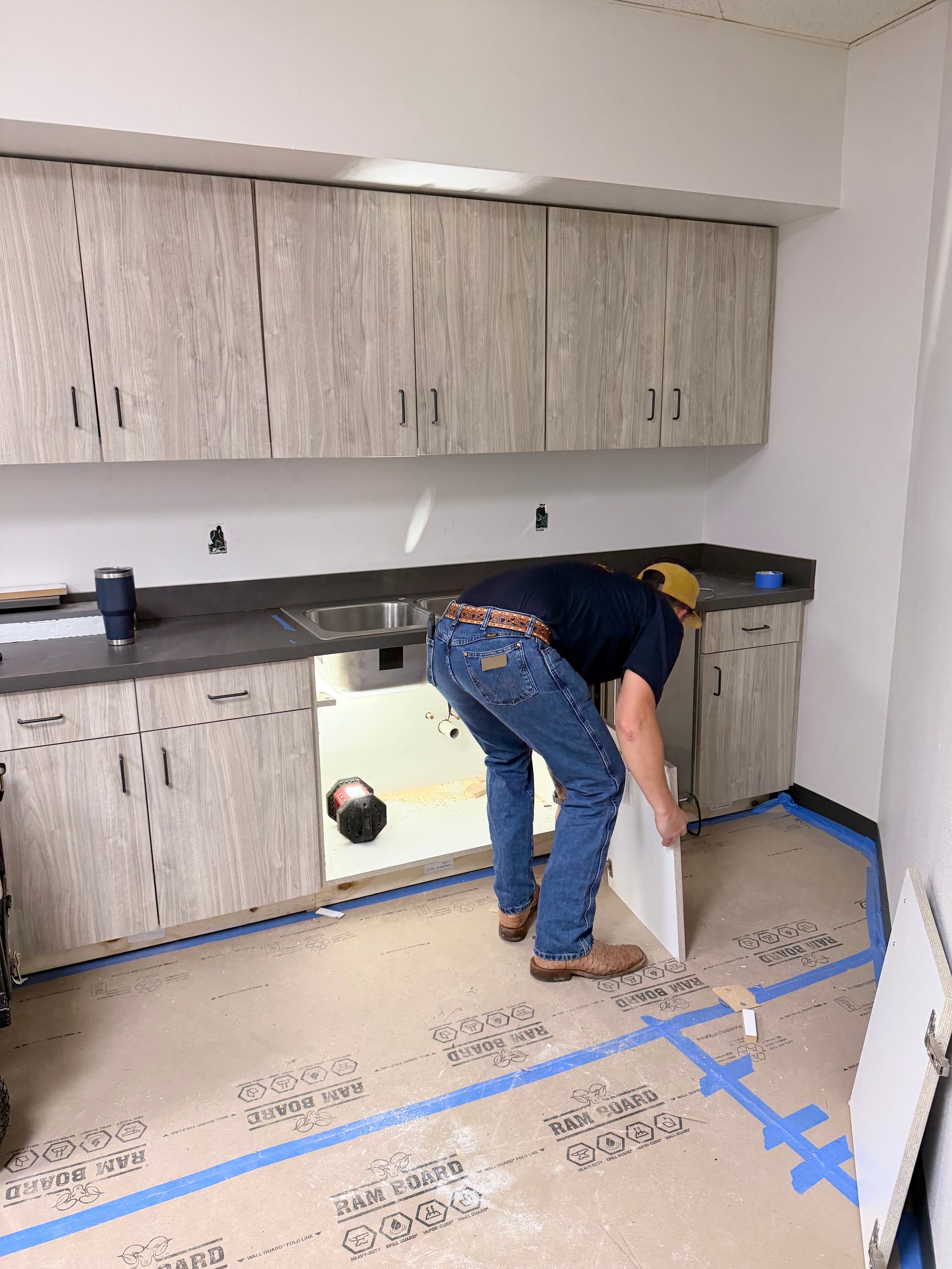 Person installing cabinets in a kitchen with blue painter’s tape and protective floor covering