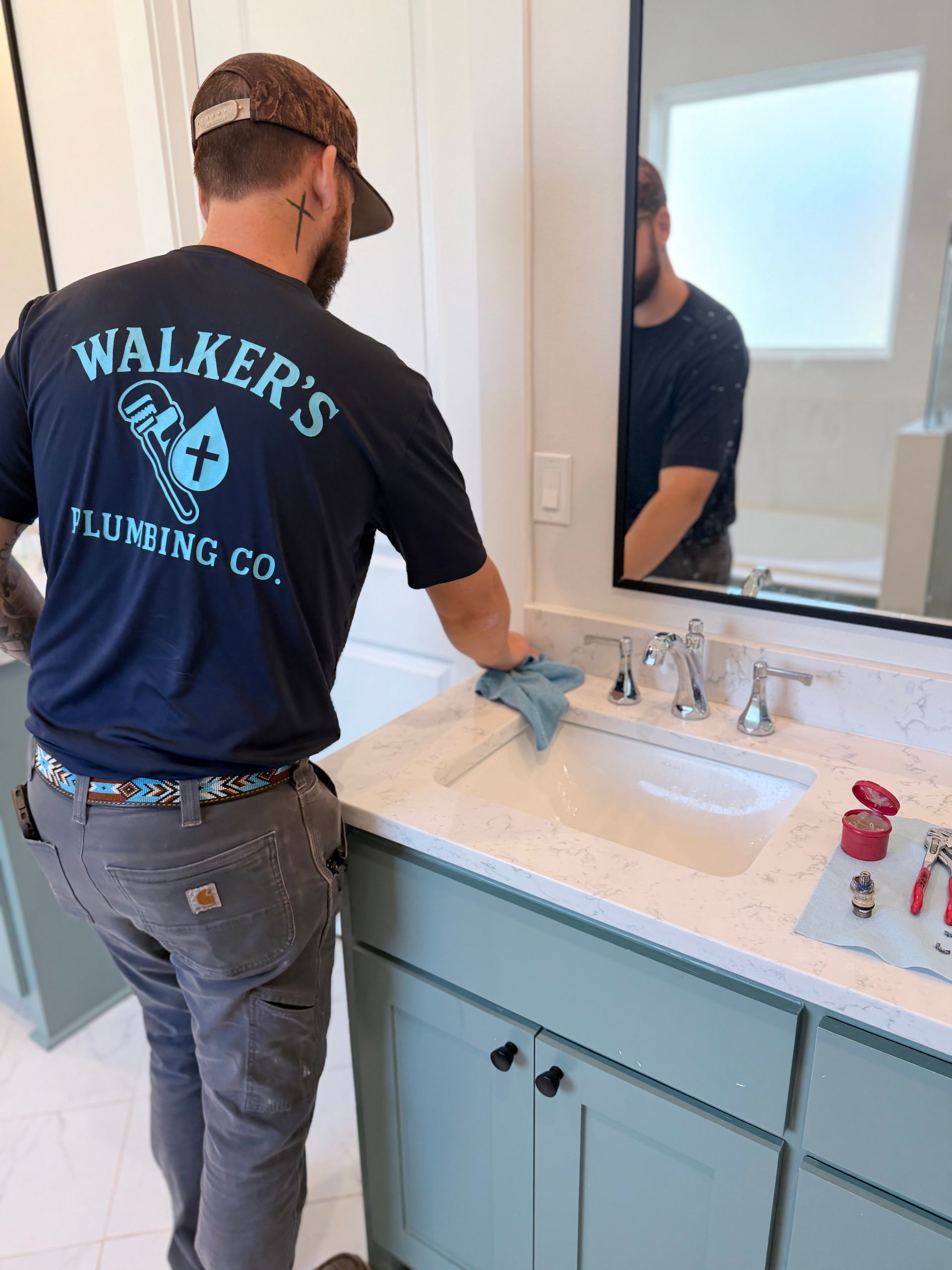 Plumber working at a bathroom sink vanity, inspecting the faucet and mirror above the counter.