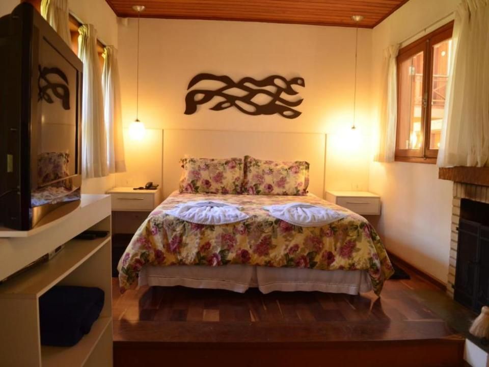 Quarto aconchegante com colcha floral, dois abajures, teto de madeira e janelas em ambos os lados.