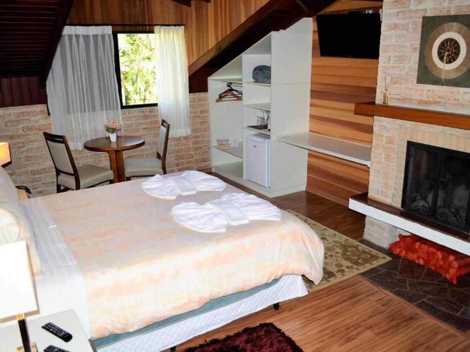 Quarto aconchegante no sótão com cama, mesinha, prateleiras e lareira ao lado de paredes revestidas de madeira.
