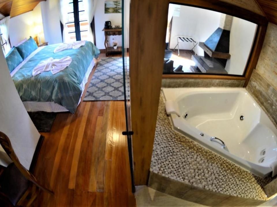 Quarto pequeno com cama e piso de madeira ao lado da pia do banheiro e banheira de hidromassagem de canto.
