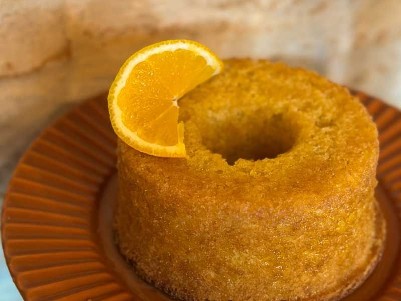 Bolo Bundt dourado com uma fatia de laranja em um prato marrom