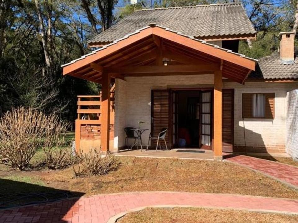 Casa pequena com varanda coberta, caminho de tijolos e árvores no quintal.