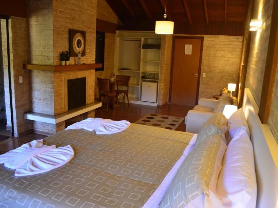 Quarto rústico e aconchegante com duas camas, lareira e uma pequena cozinha ao fundo.